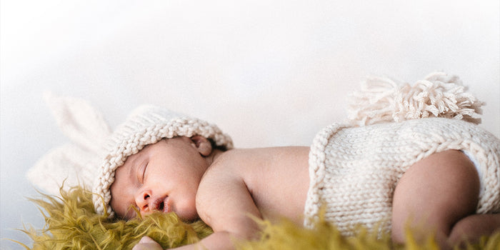 baby sleeping with a knit diaper on and a knit bunny ears hat