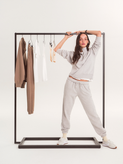 Women wearing light grey sweat suit staring at camera with arms around a clothing rack.