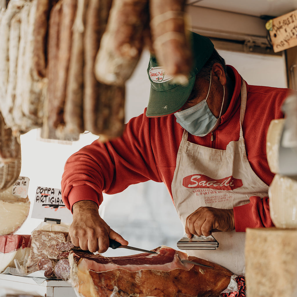 A butcher wearing a surgical mask slices cured meats.