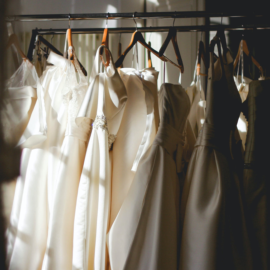 White dresses on wooden hangers in a sun-filled room.
