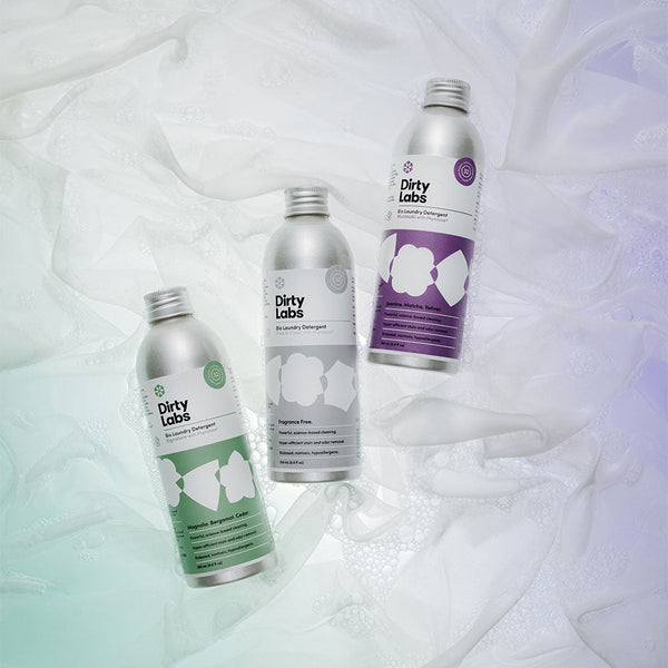 A bottle of Dirty Labs bio laundry detergent with a silver cap floats in clear, sunlit water, casting a distinct shadow and light reflections on the surface.