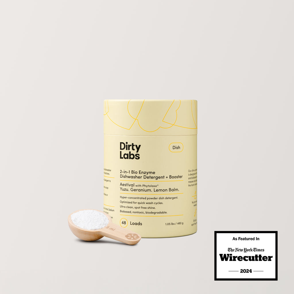 A yellow container of Aestival Bio Enzyme Dishwasher Detergent with a biodegradable formula sits on a light surface, next to a wooden scoop of white powder. The Wirecutter As Featured In 2024 badge is in the lower right corner.