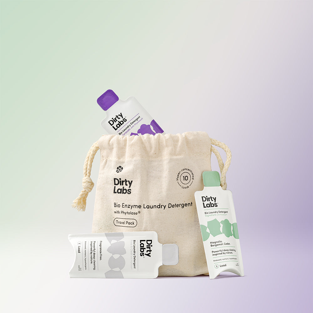 Dirty Labs single dose travel pack detergents and cloth bag against light green and purple gradient background showcasing the 10 pack travel pack product.