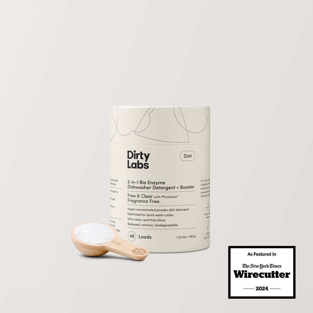 A container of Free & Clear Bio Enzyme Dishwasher Detergent with a biodegradable formula sits next to a wooden scoop of white powder. A badge highlights its 2024 feature in Wirecutter by The New York Times.