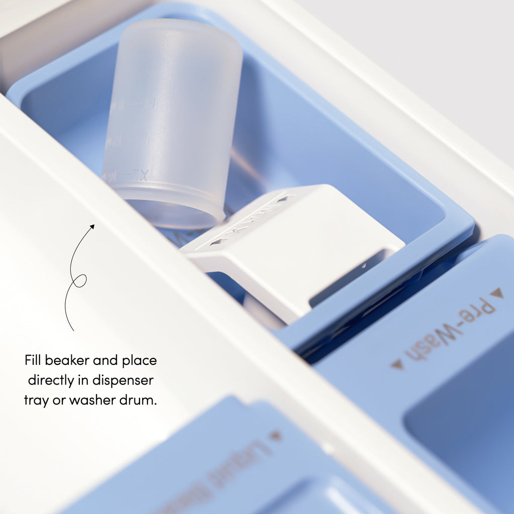 Close-up of a washing machine's dispenser tray illustrating where to place the clear silicon measuring beaker. Text instructs: Fill beaker and place directly in dispenser tray or washer drum.