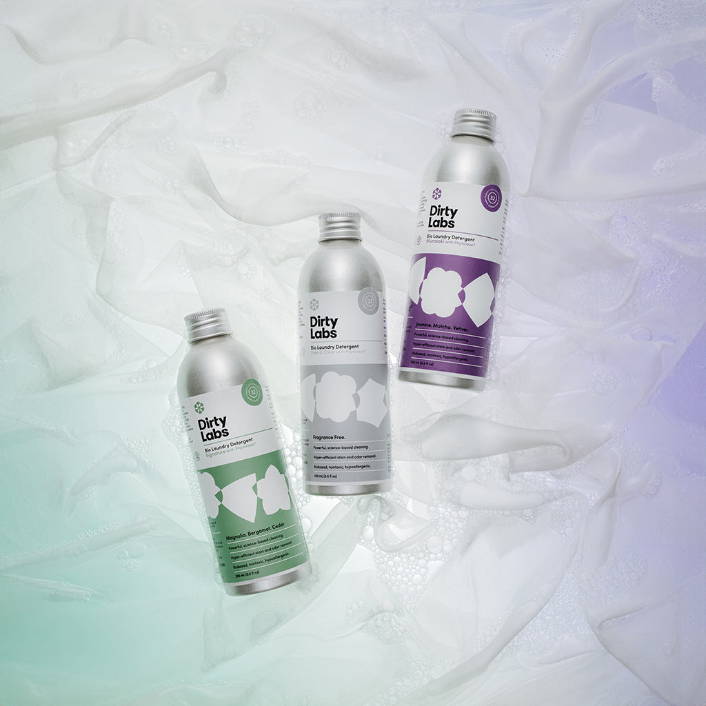 Three Dirty Labs 32 load laundry bottles on a textured light background with soap and water