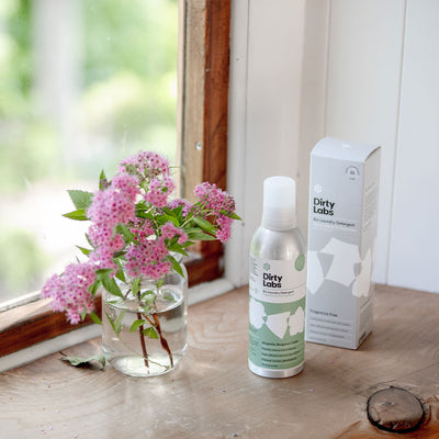 Dirty Labs detergent bottles next to pot of flowers on wood table