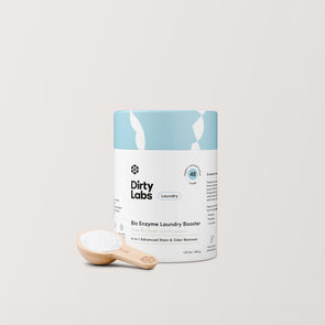 A hand displays a container of Bio Enzyme Laundry Booster. The container is a blue and white cylindrical cardboard container with labeling. The backdrop is light grey.