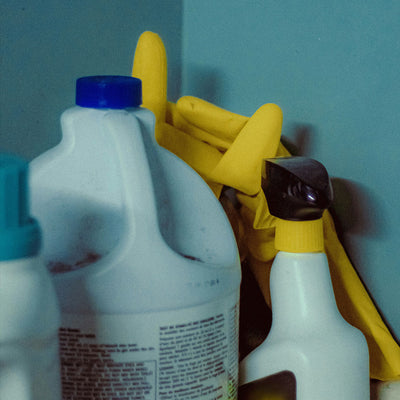 Bottle of chlorine bleach with rubber gloves against a blue wall
