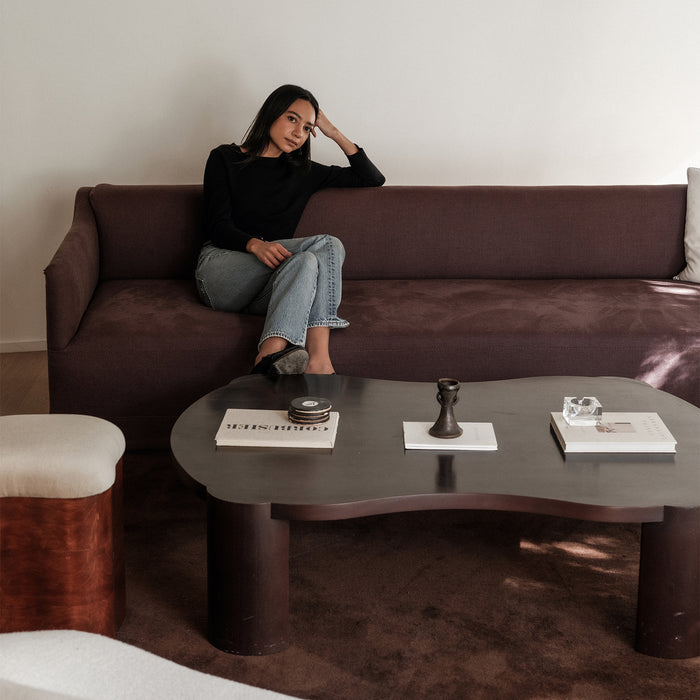 Maggie the founder of claude home  sitting on a brown sofa in a modern living room with a coffee table.