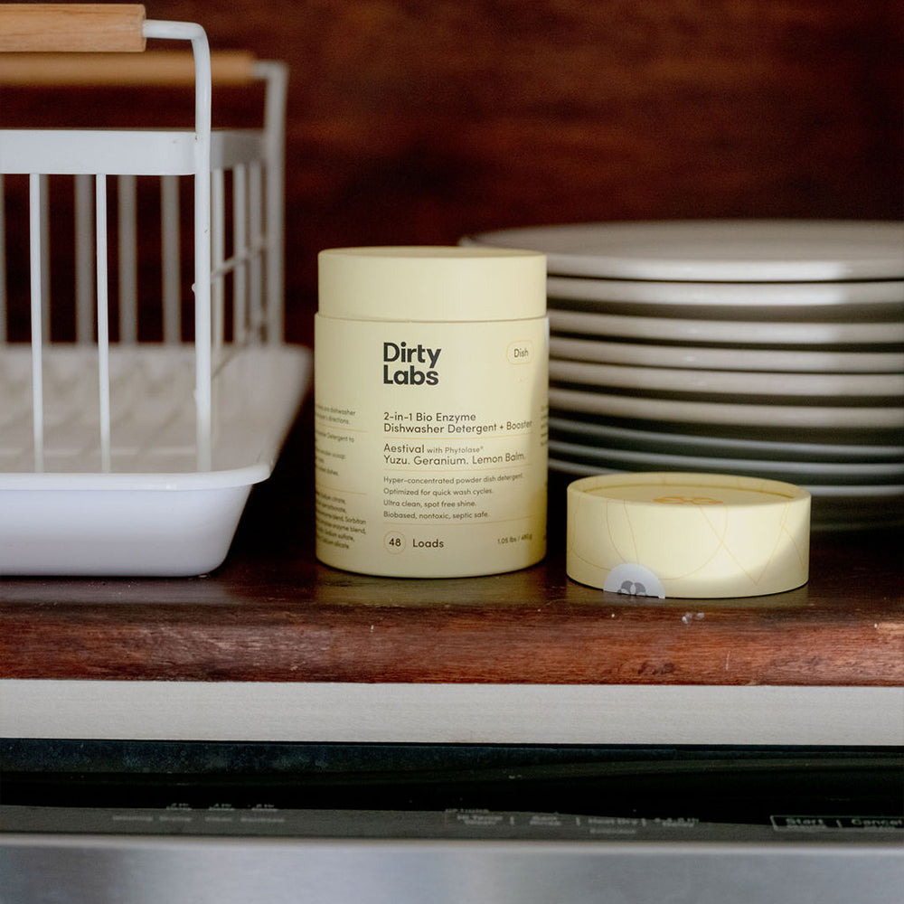 Container of 'Dirty Labs' detergent on a kitchen counter with a dishwasher in the background.