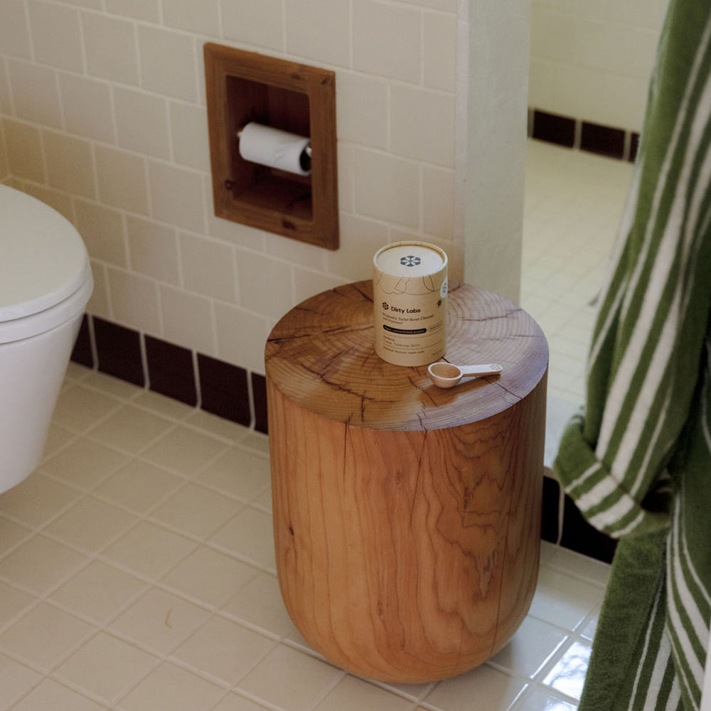 Wooden stool with a probiotic toilet bowl container and spoon in a bathroom setting