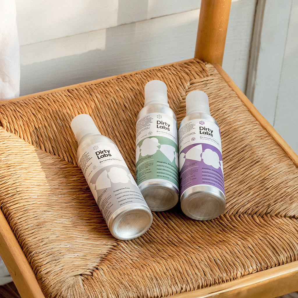 Close up of 3 Dirty Labs 32-load detergent bottles on a wood rattan chair.