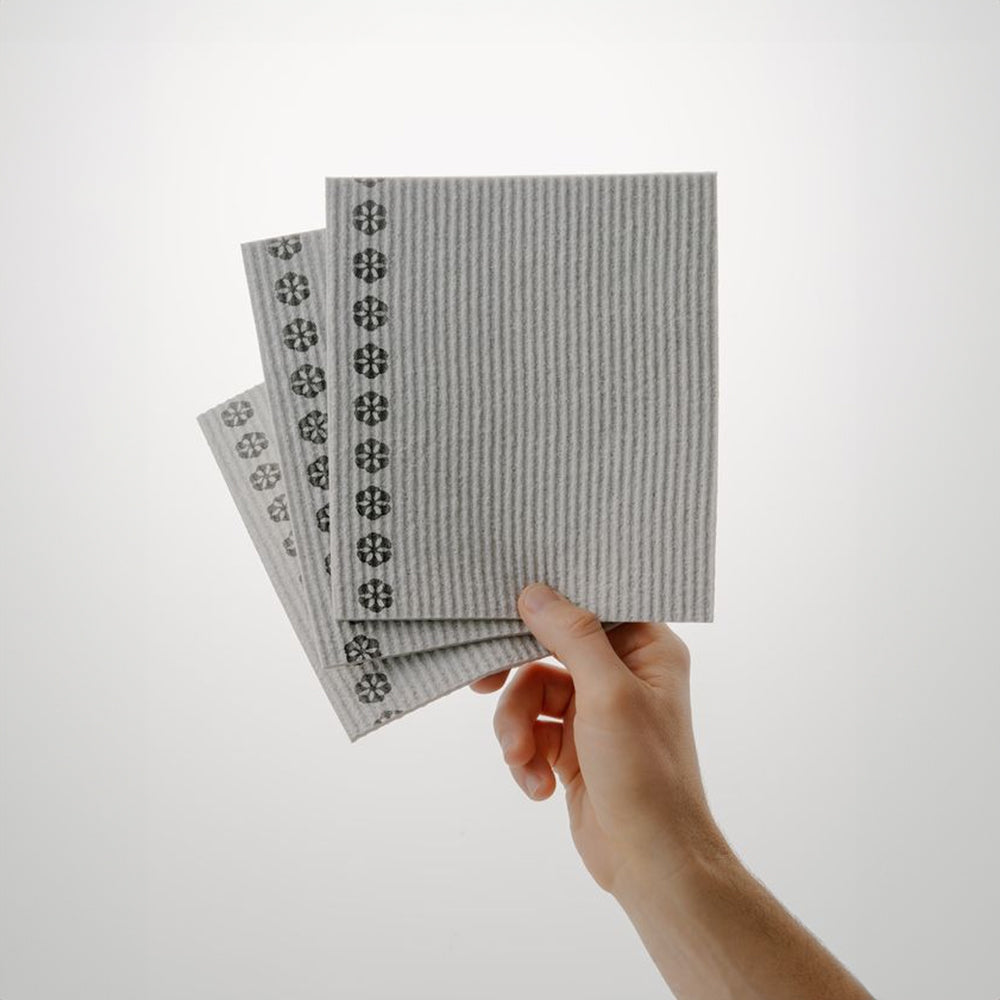 Hand holding three gray patterned german dish cloths against a light grey background