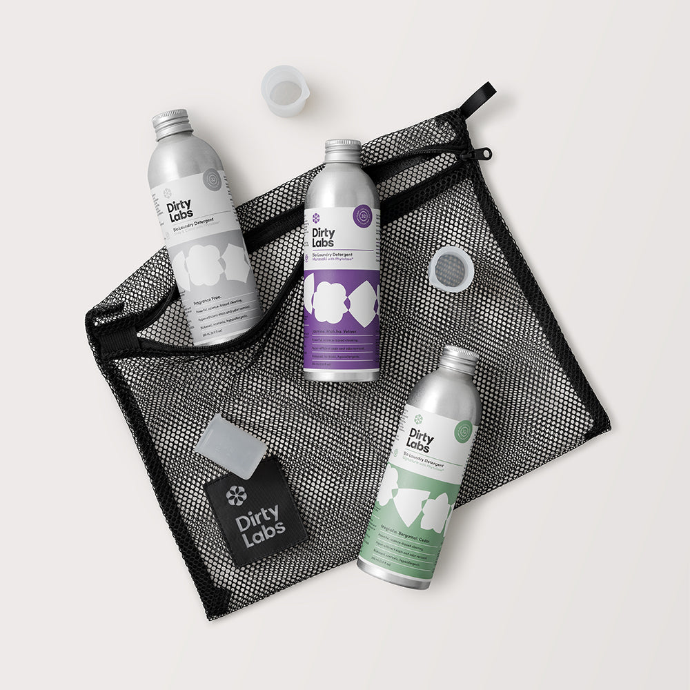 Three 'Dirty Labs' skincare products on a black mesh bag with a light grey background