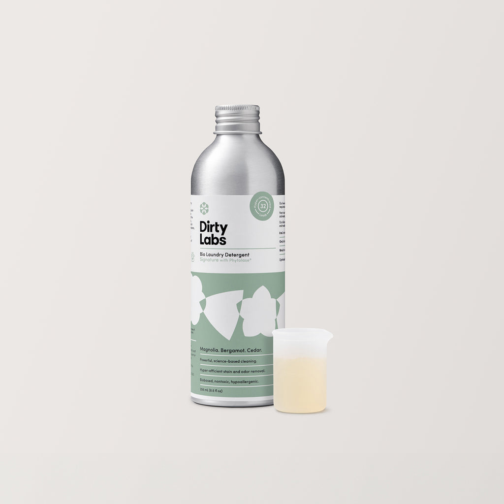 Dirty Labs bottle of 32 load Signature detergent with silicon beaker on light grey background