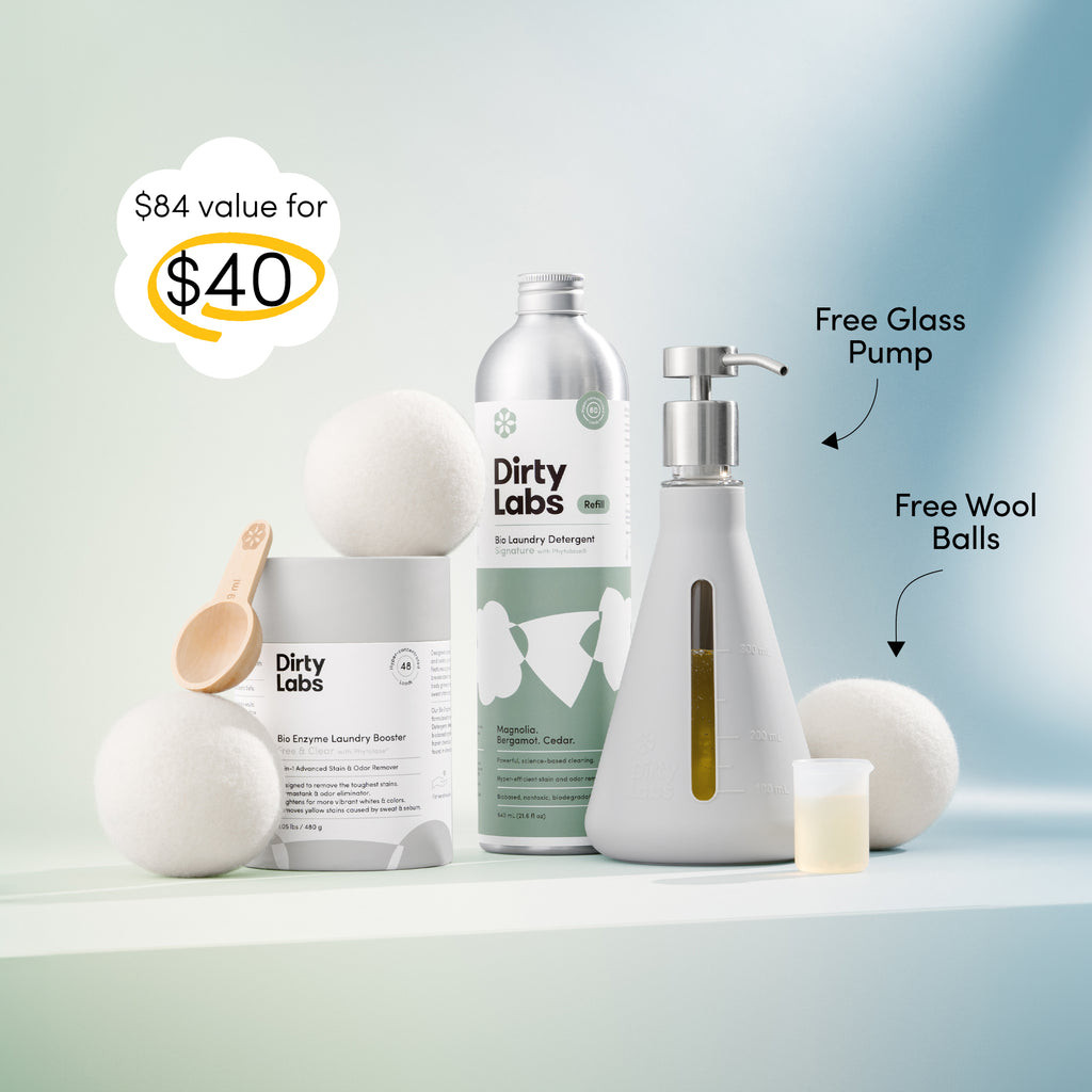 Dirty Labs 80 load signature detergent bottle with green label standing next to Booster powder container and Glass pump and wool balls against a gradient green and blue backdrop. Text on image highlights $84 value for $40.