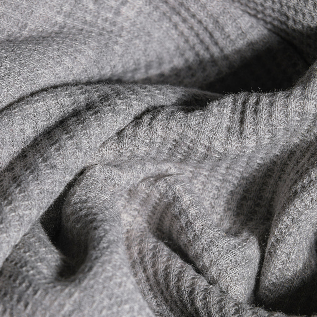 Close-up of soft, textured grey fabric with a waffle-knit and ribbed pattern, showing gentle folds and shadows.