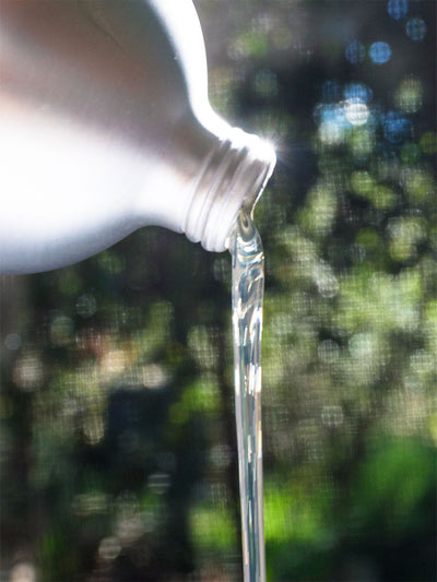 Close-up of a bottle being tilted to pour detergent with a blurred green background
