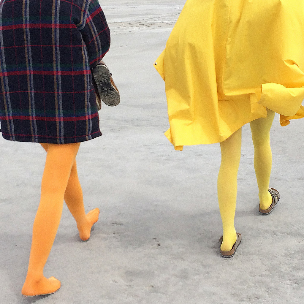 Close up of the legs of two people walking on the sand in bright, colorful clothing.