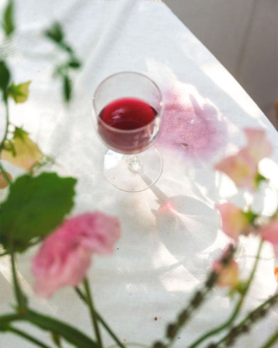 Glass of red wine on a white surface with pink flowers and green leaves.