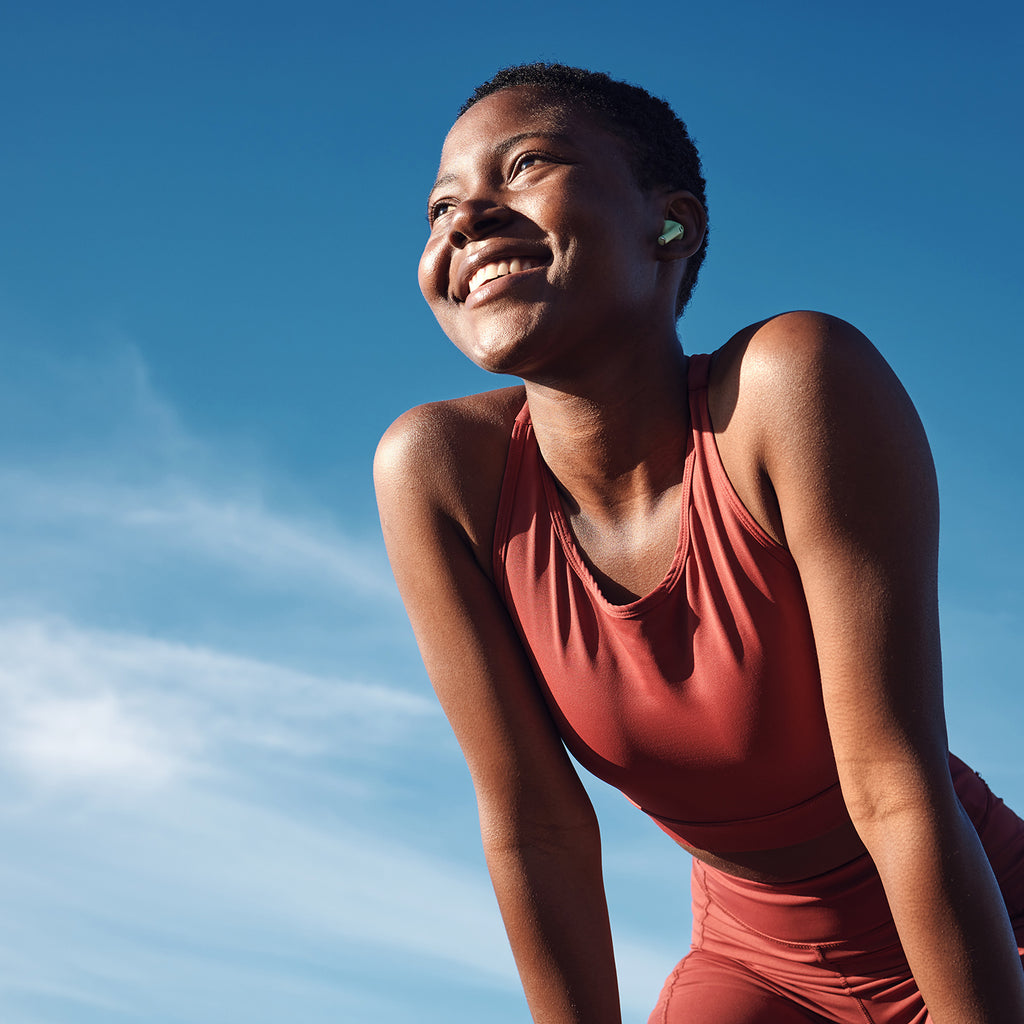 A woman in a matching red workout outfit is bent over with her hands on her knees and smiling. The photo is shot from below so the background is  just a bright blue sky with one wispy cloud.